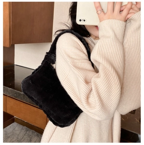 Détail d'un sac à bandoulière en fausse fourrure noire porté avec un pull en maille blanche