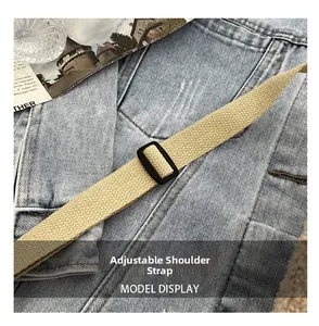 Détail d'une bandoulière en toile beige ajustable avec boucle noire sur du denim