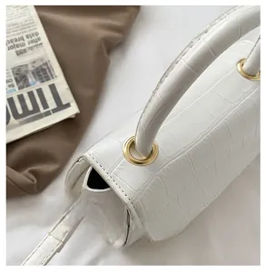 Detail shot of white crocodile embossed leather bag showing stitching and golden hardware