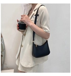 Detail of minimalist black hobo bag with gold hardware worn by model in beige suit