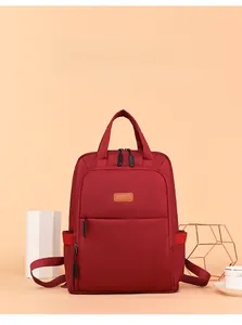 Close-up of red Oxford fabric backpack showing brown leather label and front zipper pocket
