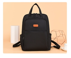 Detail view of the black waterproof Oxford fabric texture and brown leather patch on the backpack