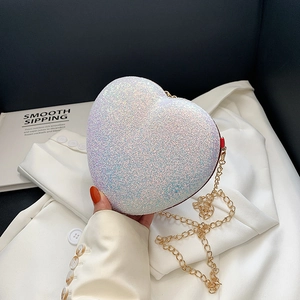Glittery heart-shaped crossbody bag with gold chain strap held against a blazer