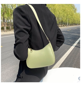 Avocado green leather baguette bag with crescent design worn by model over shoulder