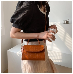 Detail of a brown crocodile-patterned PU leather small square crossbody bag on model