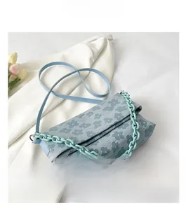 Détail d'un sac bandoulière fleuri bleu avec grosse chaîne verte et texture de tissu