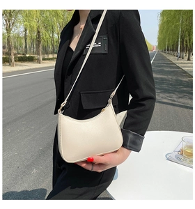 Close-up of a cream minimalist saddle bag worn by a model in a casual outdoor street setting