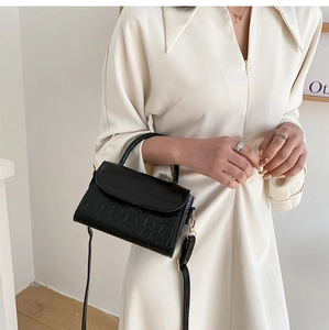 Detail of black crocodile texture handbag with gold hardware on a model's shoulder