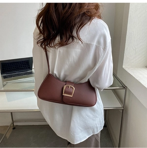 Detail of dark chocolate crescent underarm bag with a gold buckle on white shirt