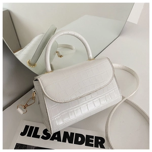White faux crocodile texture handbag with gold hardware and shoulder strap in a minimalist setting