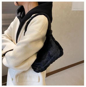 Vue latérale du sac à épaule en fausse fourrure noire douce sur un manteau blanc