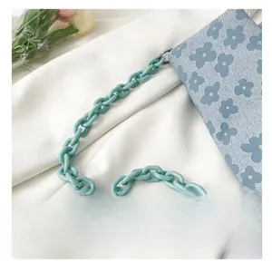 Détail du sac bleu clair gaufré de fleurs avec une grosse chaîne en plastique verte