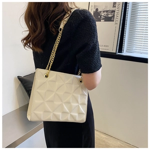 Detail of white geometric embossed tote bag with gold chain strap on model shoulder