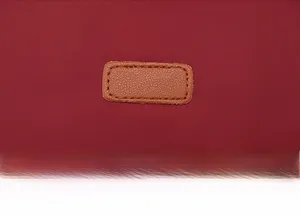 Detail of burgundy oxford fabric and brown leather label with reinforced stitching