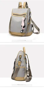 Detail view of grey nylon backpack with tan faux leather trim and cat pendant