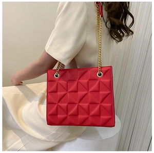 Detail of red tote bag with 3D geometric relief texture and golden chain strap