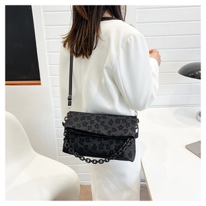 Détail du sac bandoulière noir brodé de fleurs avec chaîne sur un blazer blanc