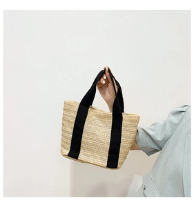 Detail of hand-woven straw bag featuring contrasting black canvas straps and texture