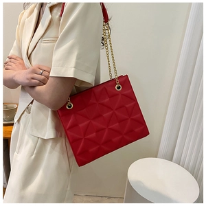 Detailed close-up of 3D geometric quilted pattern and gold chain strap on a red tote bag