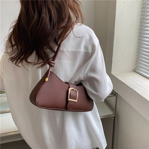 Minimalist dark brown leather shoulder bag with a gold buckle shown on a model