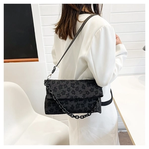 Détail du sac à bandoulière en jacquard noir avec des motifs floraux et une chaîne