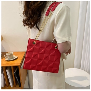 Detail of red quilted tote bag with gold chain strap and geometric square pattern texture