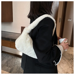 Sac hobo en fausse fourrure blanche porté sur l'épaule sur un blazer noir chic