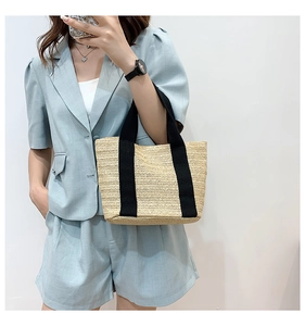 Detail shot of straw tote bag featuring herringbone weave texture and black ribbon straps
