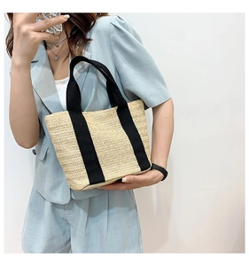 Detailed view of woven straw tote bag with black canvas straps for summer beach style