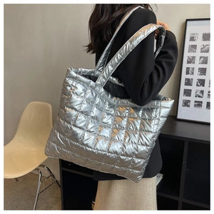 Detail of silver metallic quilted tote bag with wide shoulder strap worn by a model