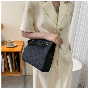 Detail of geometric quilted black tote bag with gold chain strap on shoulder