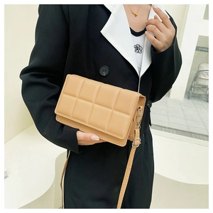 Detail of light brown quilted crossbody bag featuring textured square stitching and silver hardware