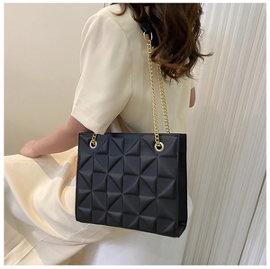 Detail of black quilted tote bag featuring geometric patterns and golden chain straps