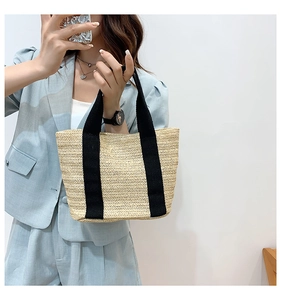 Close-up of straw woven tote bag with durable black canvas handles for summer beach use