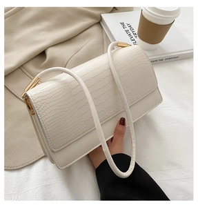 Detail of beige crocodile pattern texture and golden hardware on a baguette shoulder bag