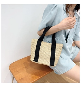 Detailed view of the straw weave texture and contrasting black canvas handle on the bag