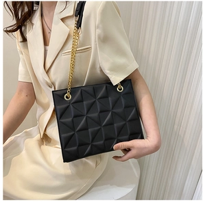 Detail of a black crossbody bag with 3D geometric texture and golden chain strap
