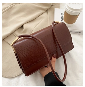 Detail of crocodile embossed leather flap on brown baguette bag with gold hardware