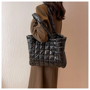 Detail of a black quilted puffer tote bag with square stitching and a thick shoulder strap