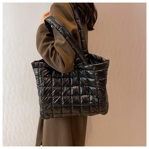 Close-up of black glossy quilted tote bag with wide shoulder strap and waterproof texture