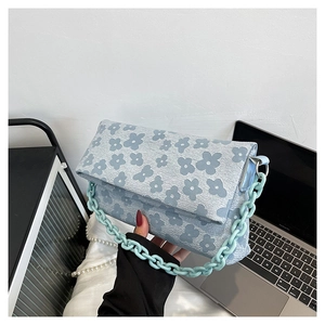 Détail d'un sac bandoulière bleu clair à fleurs avec une grosse chaîne en acrylique