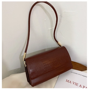 Detail of burgundy crocodile pattern leather texture on a minimalist shoulder bag