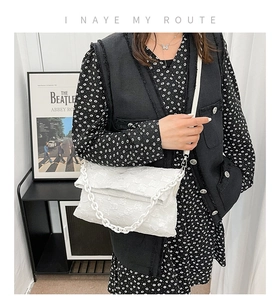 Detail of white textured shoulder bag featuring chic chain strap and woven flap design