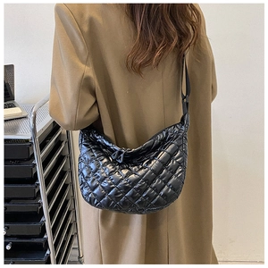 Side view of black quilted shoulder bag with glossy finish on a model wearing a khaki coat