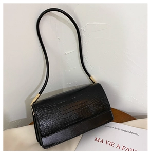 Detail of black crocodile embossed leather bag with cylindrical gold metal hardware