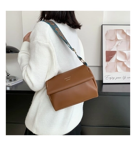Détail du sac à rabat en cuir marron avec surpiqûres blanches et bandoulière tissée