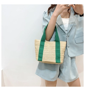 Detailed texture of handwoven straw tote with contrasting green fabric handles