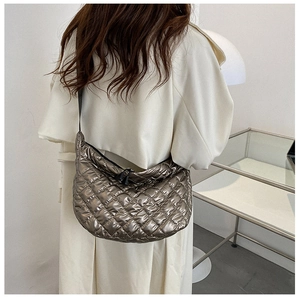 Detail view of metallic bronze quilted cloud bag worn over a beige trench coat