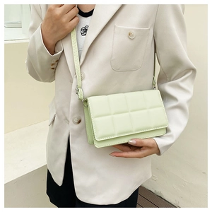 Close-up of light green quilted crossbody bag shown on a model in a beige suit