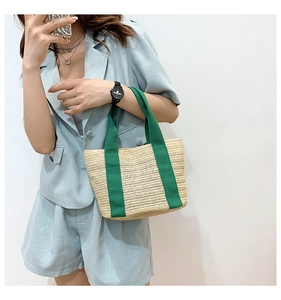 Detail of hand-woven straw tote bag with V-shaped texture and green canvas straps